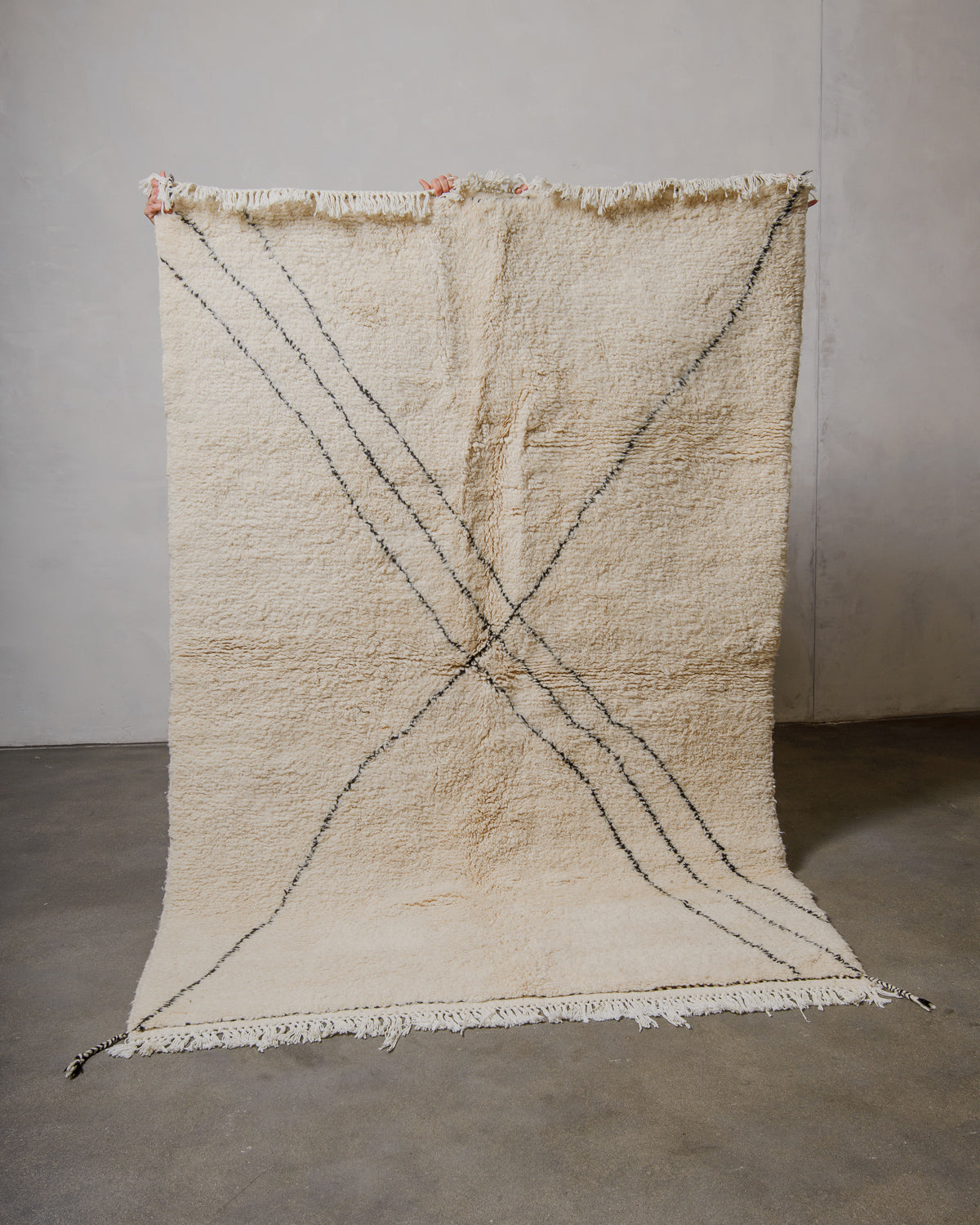Cream wool Berberlin Beniourain rug being held up by hands in front of a plain wall.